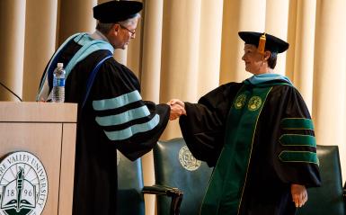Two dignitaries are commencement shaking hands.