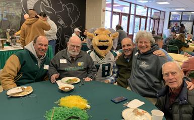 Older alumni sitting around a table with the DelVal mascot.