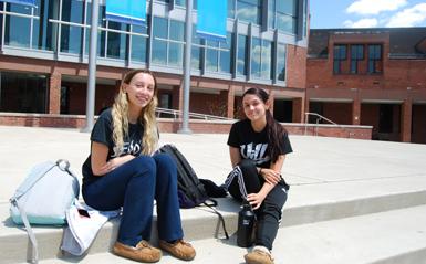 Two female students sitting on the steps of the campus on a sunny day