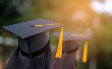 Two people graduate caps with tassels against the sunset.
