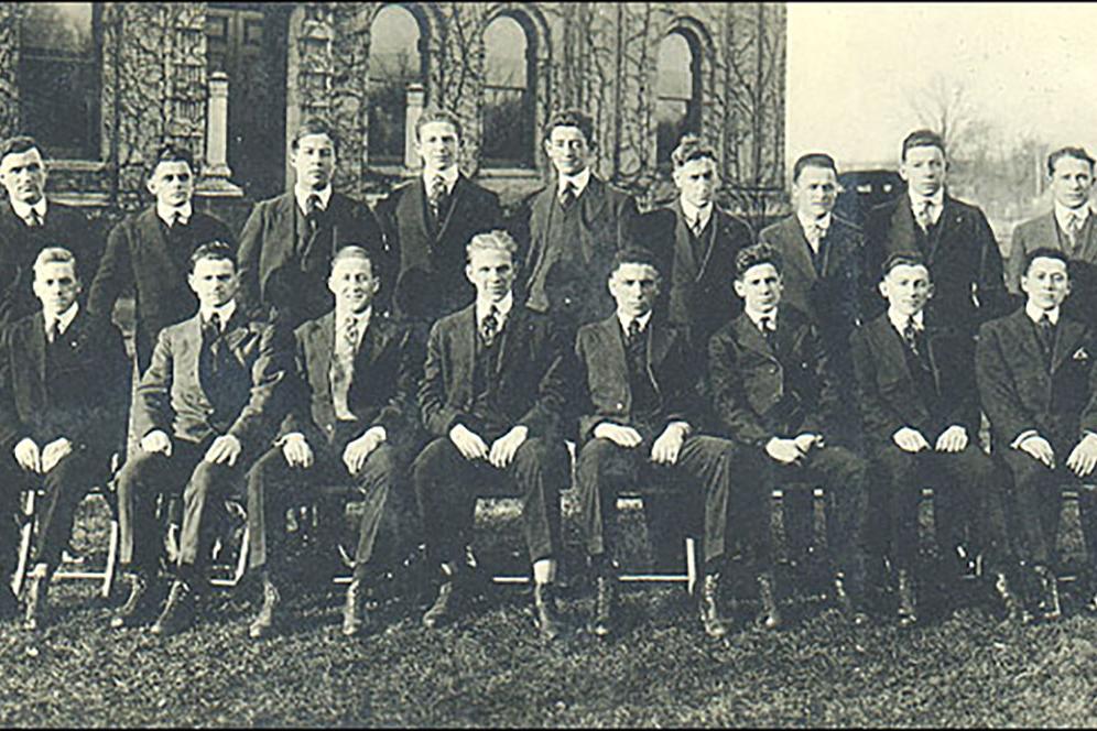 A group of about 17 men lined up in two rows at graduation ceremony.