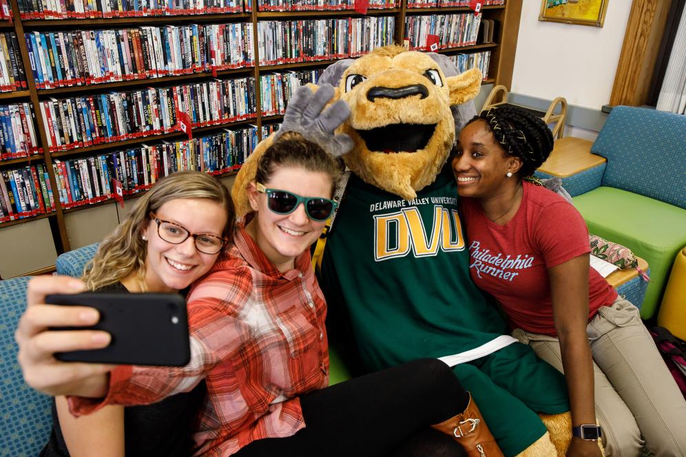 Three students taking a selfie with mascot