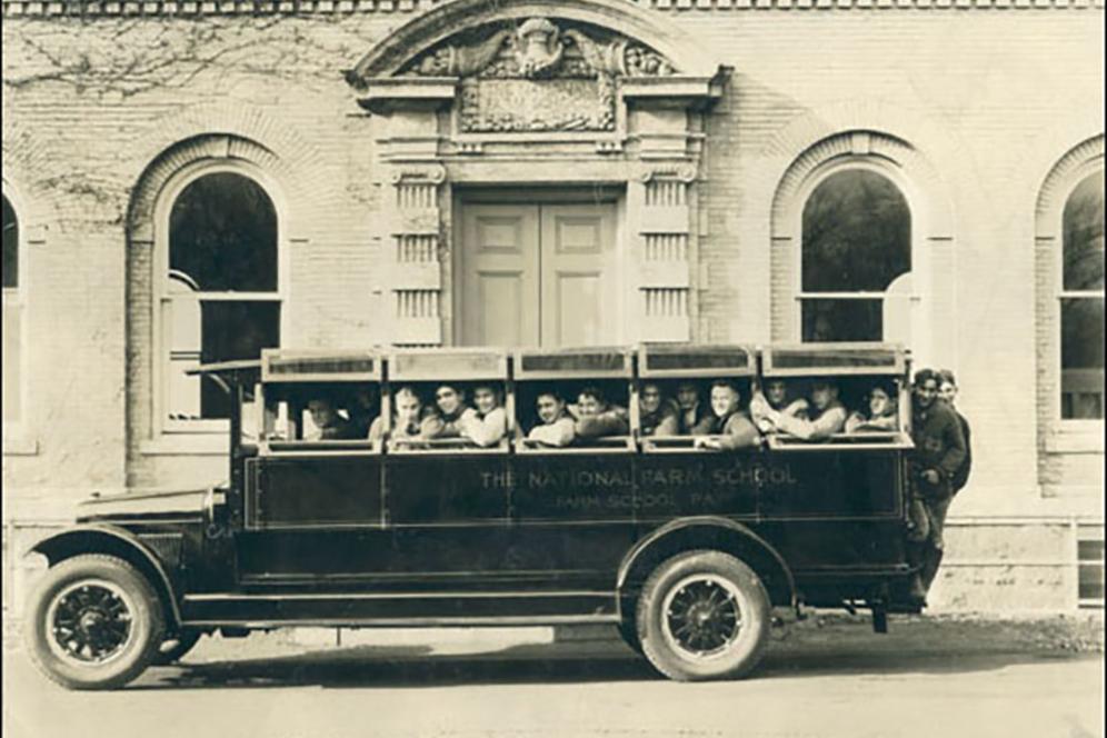 Very old bus full of students on a dirt road.