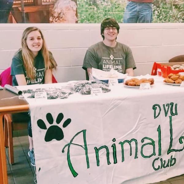 Two students sit at the animal lifeline club table at an activities fair.