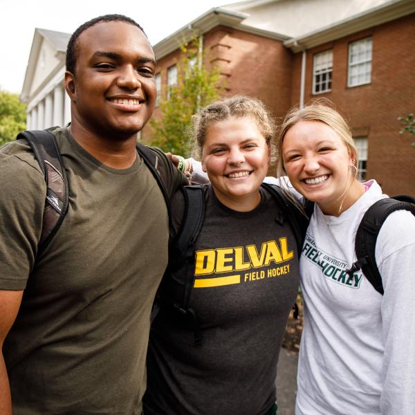 Three students stand with arms around each other.