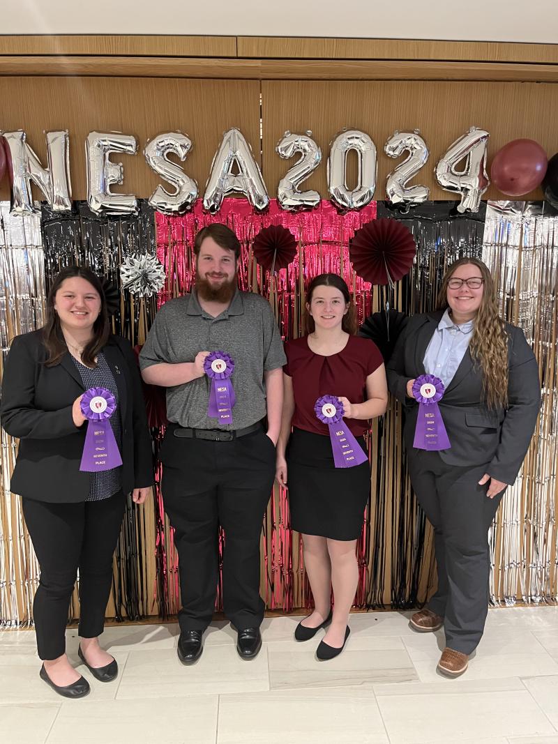Team E: 7th place judging team, three women and one man holding up a purple ribbon.