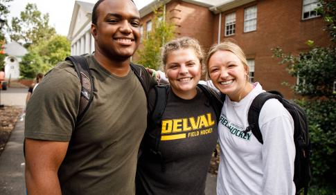 Three students stand with arms around each other.