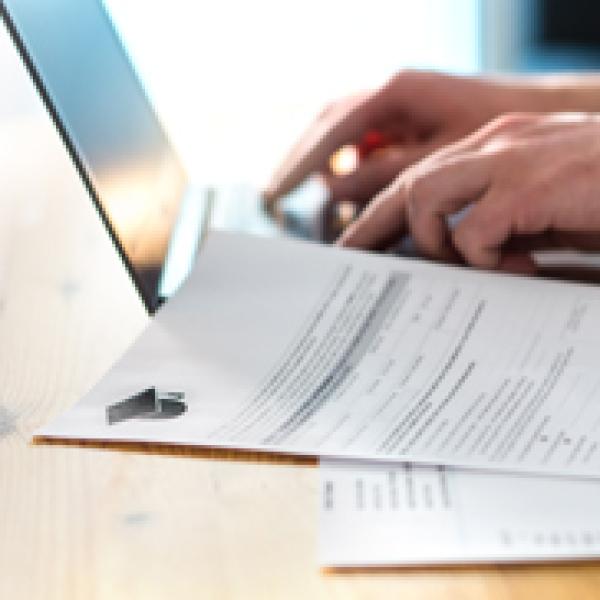 hands on a laptop with a form nearby.