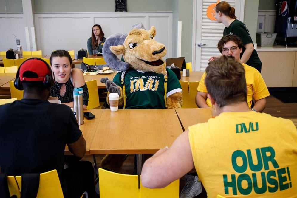 School mascot surrounded by students at lunchtable.