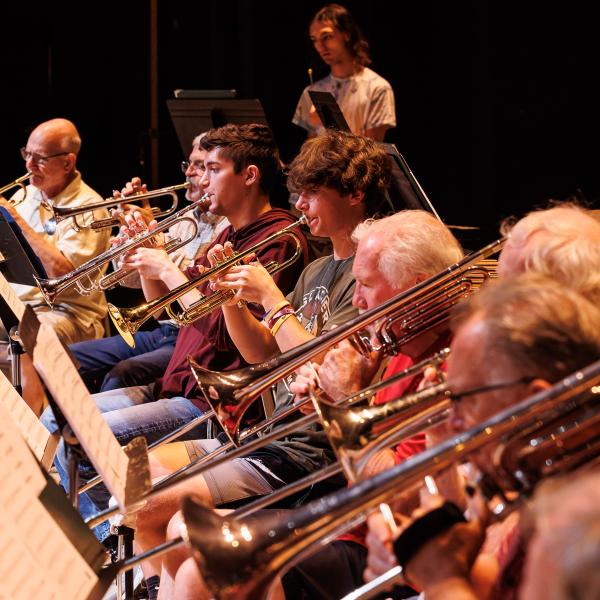 Musicians are seated next to each other reading sheet music while playing the saxophone. 