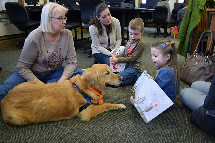 A therapy dog next to a child who is reading a book.