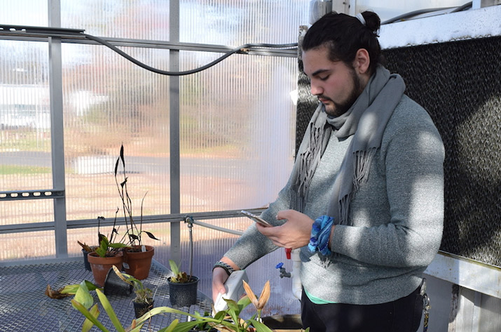 A student collects data in the greenhouse using a small, handheld device. 