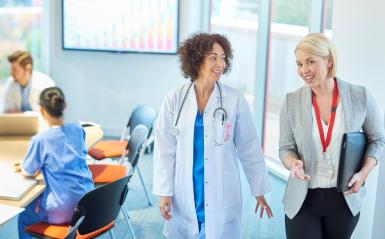 A female physician walking and talking with a female healthcare administrator.