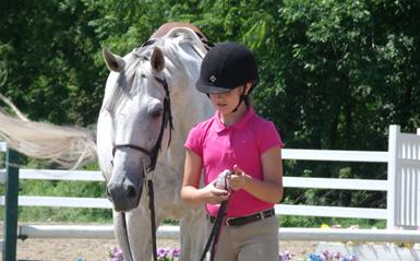 a girl in riding gear leading a white horse 