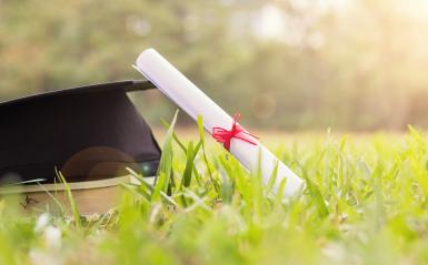 A diploma and graduation cap in the light.