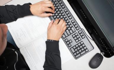 Hands on a keyboard with a book nearby.