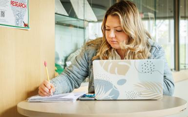 A student is working on a laptop and notepad with pencil in hand.