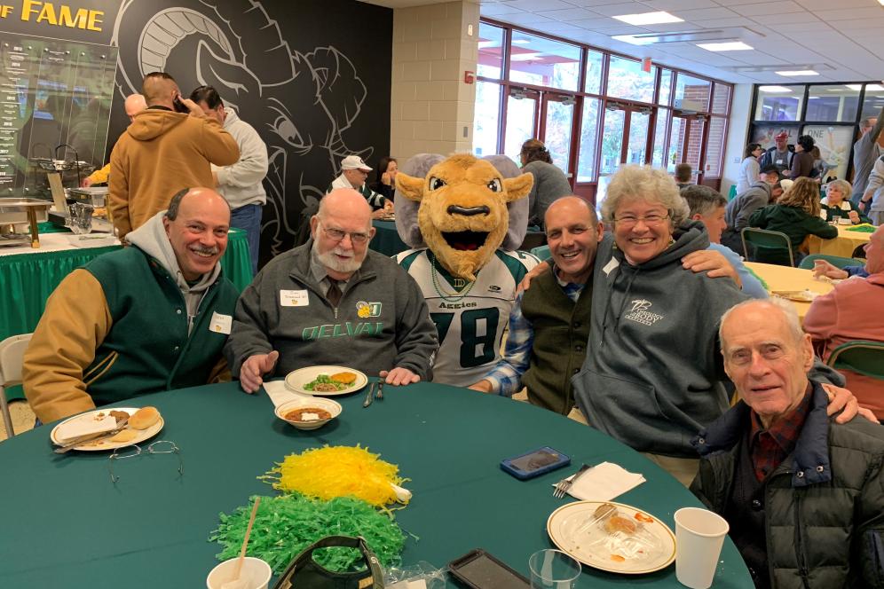 A group of alumni sitting around a table with the mascot.