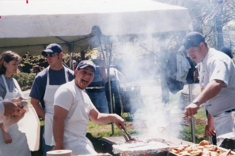 People are grilling food at a-day in a historic photo. 