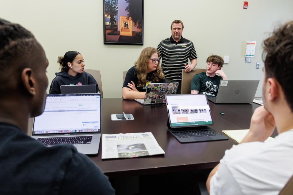 Jeff Wehrung with five students in a conference room having a discussion.