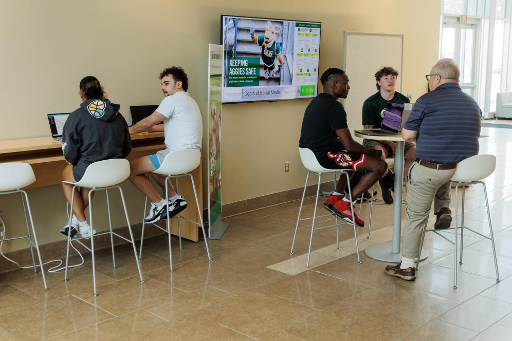 Lance Hill talking with four students infront of a computer in the Life Sciences Building.
