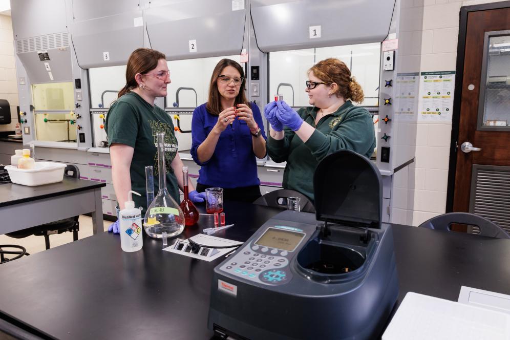 Melissa Langston in the chemistry lab with two students working with beakers.