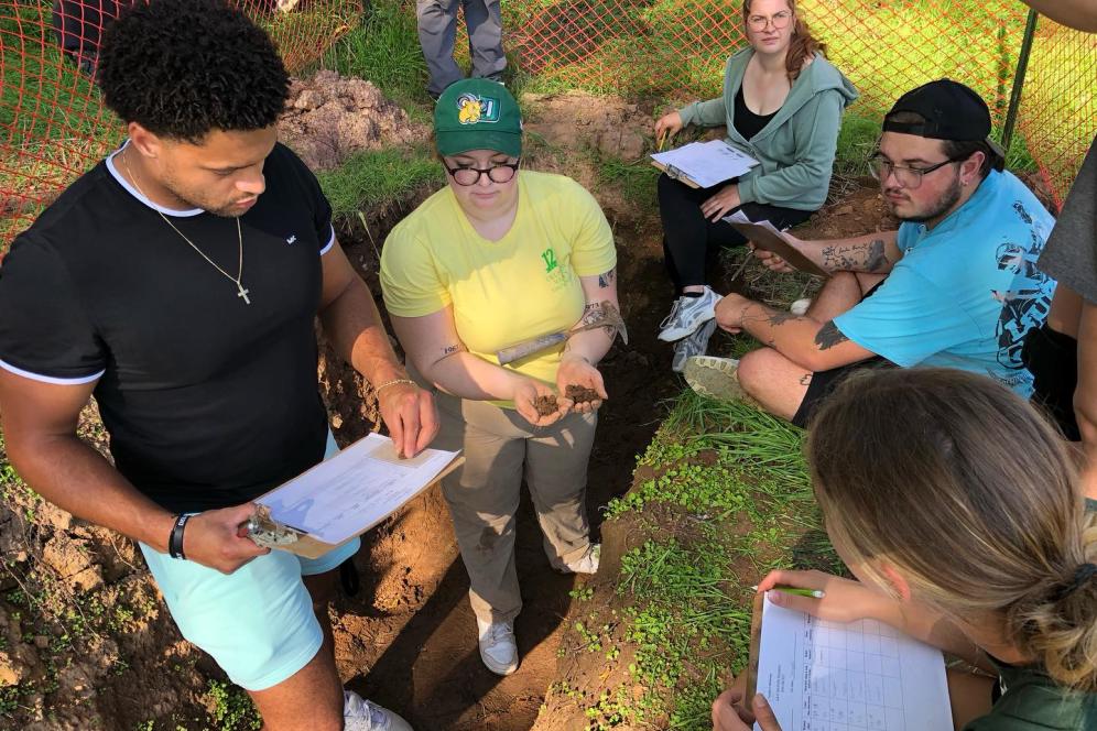 Five soil students are working in a soil pit with notebooks.