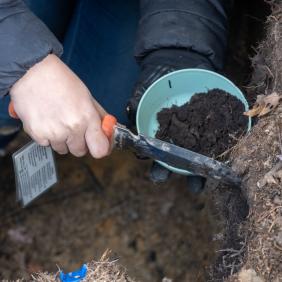 A closeup photo of a student scraping soil for a sample.