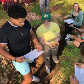 Students are in a soil pit, analyzing soil samples.