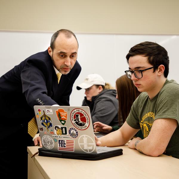 A professor and a student reviewing work on a laptop.