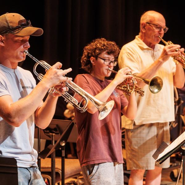 Three people playing the saxophone on stage in casual clothing. 