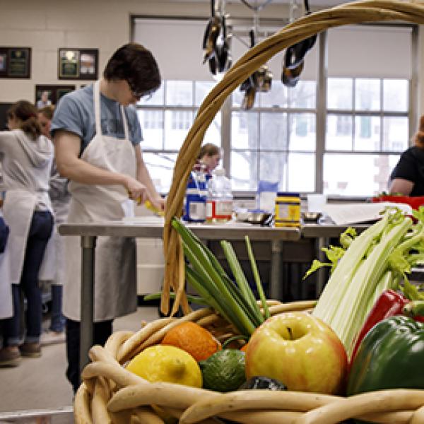 student working in a commercial kitchen with fruits and vegetables in the foreground